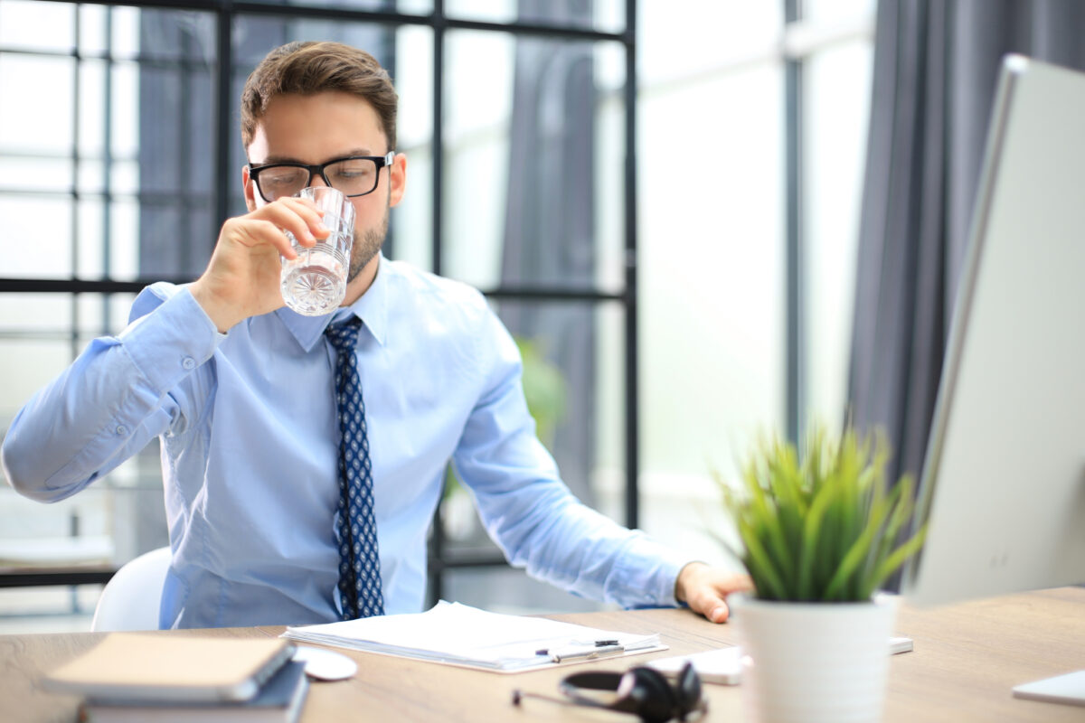 Geschäftsmann am PC trinkt Wasser im Büro