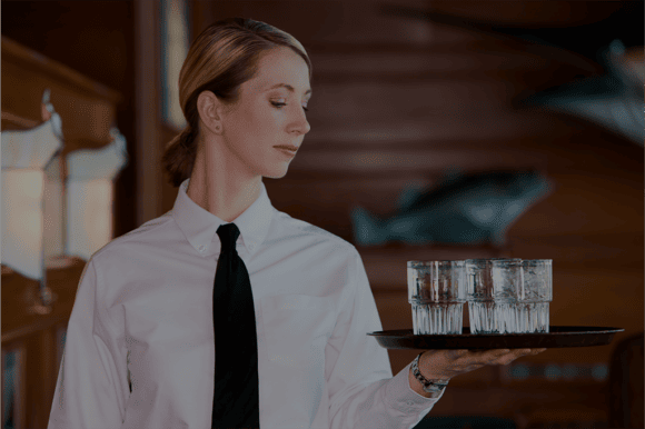Eine junge Kellnerin im Restaurant trägt ein Tablett mit Wassergläsern gefüllt mit Eauvation Sprudelwasser