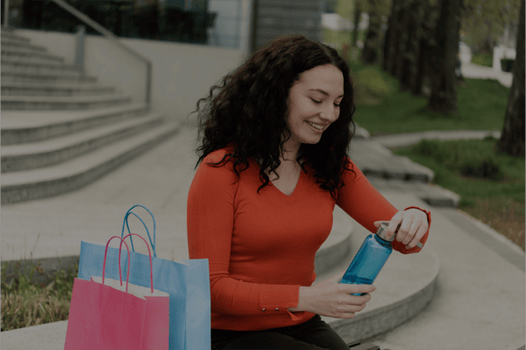 Eine Frau macht eine Pause während dem Shoppen und trinkt Wasser aus einer Trinkflasche