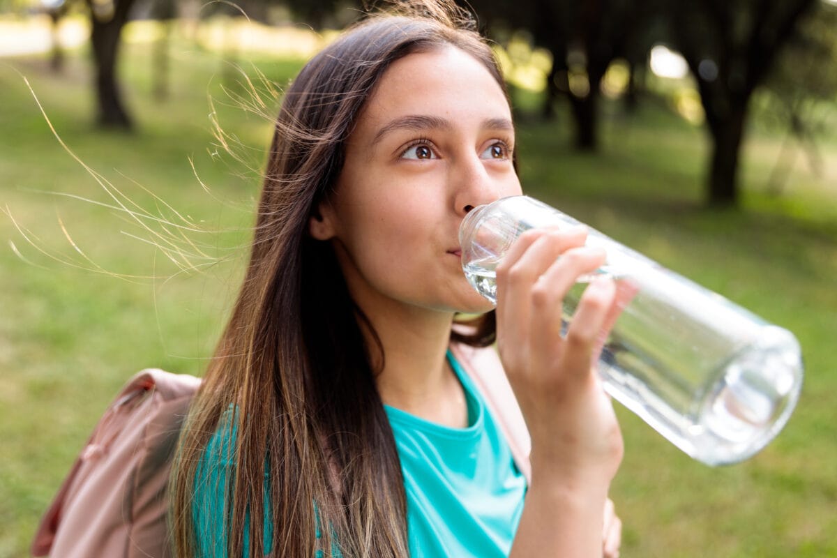 Junges attraktives Mädchen trinkt Wasser aus einer Glasflasche von Eauvation