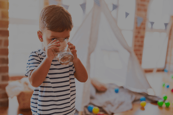 Ein Schulkind in einer Schule hält mit beidenn Händen ein Wasserglas und trinkt darauf kühles Eauvation Wasser